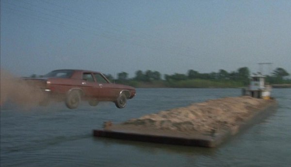 Хал Нийдъм, обичайният дубльор на Бърт Рейнолдс, прави една от най-великите каскади в "Бялата светкавица" - макар че нещата не минават точно по план. Идеята е колата - Ford LTD - да скочи от брега върху плаваща в реката баржа. Но макар Нийдъм да изпълнява всичко по часовник и да отскача от рампата с точно 130 км/ч, колата се приземява само наполовина върху баржата. Но пък така е още по-ефектно. 
