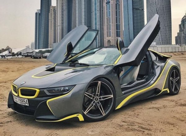 Разбира се, историята на Blondie и суперавтомобилите започва едва, след като се мести в Дубай, едно от малкото места на Земята, където Porsche 911 и Alfa Romeo Giulia Quadrifoglio се считат за базови коли. След като се закрепи в новата си кариера, Алекс си купува BMW i8 и го декорира със сиво-черна цветова схема и неонови жълти акцентиращи ивици.