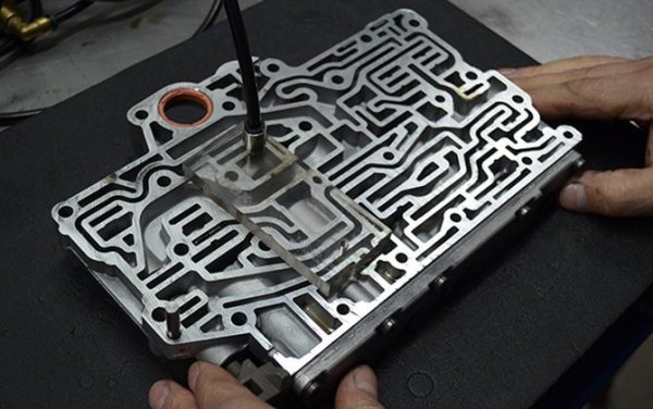 Корпусът на клапана е много важна част, която представлява метална плоча, състояща се от главни хидравлични канали с набор от клапани и сензори за управление. Той служи за разпределяне на налягането на трансмисионната течност вътре в самата кутия, което е необходимо за навременна смяна на предавките.

По време на работа на агрегата в него възниква естествено триене на механичните елементи, което води до запушване на запушване на трансмисионното масло с прах и метални абразиви. Постепенно продуктите, образувани от износването, се утаяват вътре в корпуса на клапана, което в крайна сметка води до окисляване на соленоидите. Блокът е надежден и може да изкара дори 10 000-20 000 км, но ремонтът не бива да бъде отлаган