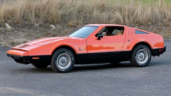 Малкълм Бриклин е човекът, който натрапва Subaru 360 и Yugo на американските купувачи и ако това не е доказателство за злонамерени намерения, не знаем какво друго може да е. Единственият му опит да направи собствена кола е пластмасово изглеждащият Safety Vehicle 1 и колата е ужасна поради много причини, включително визуално. Оборудвана е с малки странични процепи, колкото да стреляш с арбалет, вместо със стандартните стъкла, а джантите са с дизайн  на турбинни перки.

Качеството на сглобяване е ужасно: панелите на каросерията се изкривяват (често преди да бъдат прикрепени към шасито), скритите фарове обичат да остават скрити, колите протичат като направени от тензух, а вратите тип „криле на чайка“ се огъват или чупят под собствената си тежест.
