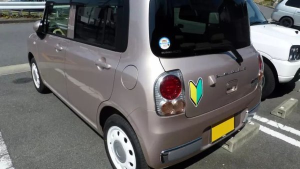 Жълто-зелената стрелка върху автомобила означава - Shoshinsha (Шошинша) или Wakaba (Уакаба), тоест, че шофьорът е начинаещ. И не е само индикатор за стажа зад волана, а част от JDM културата. В Япония се превърна в обичайна практика този символ да се поставя върху автомобилите като закачливо намигване към автентичността на JDM. Дори опитни шофьори го правят. Не само че не е срамно, но дори и почтено. Стикерът се превърна в културен шифър сред феновете на JDM по целия свят.
